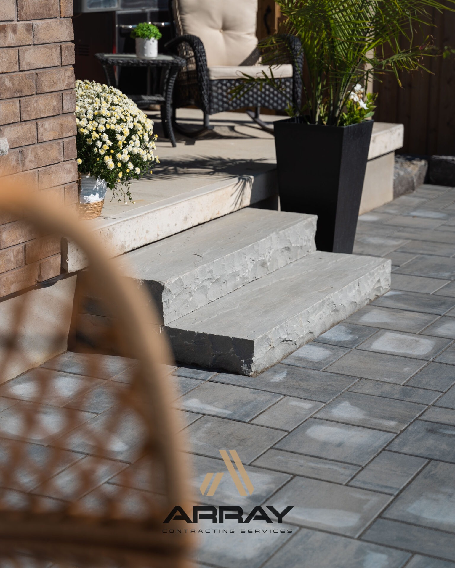Outdoor patio with stone steps, wicker chairs, plants, and a flower pot. 