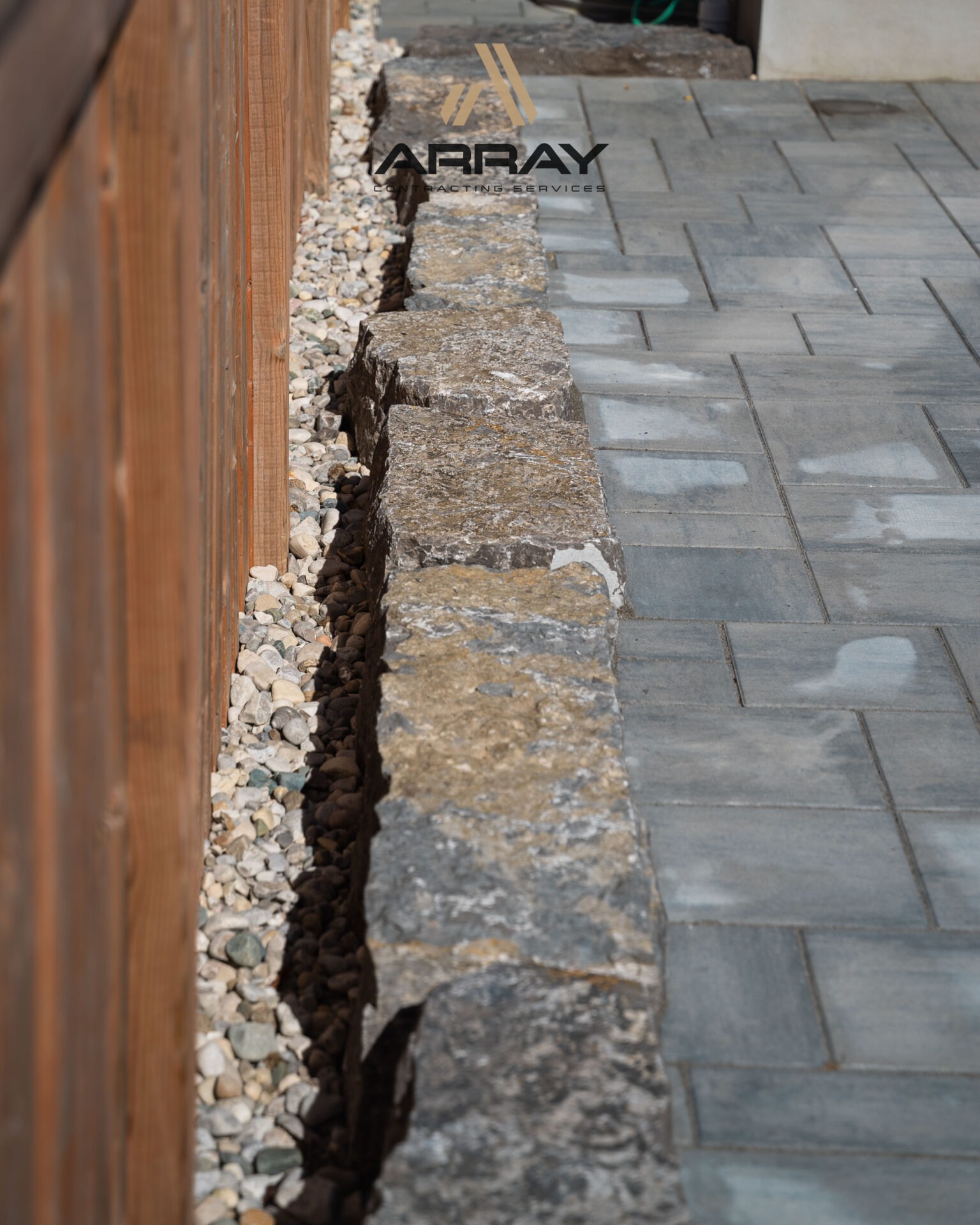 Stone pathway bordered by gravel and wooden fence, featuring 
