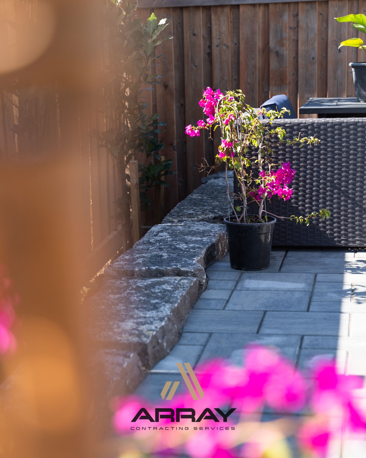A patio with a potted plant and wicker furniture, set against a wooden fence. The Array Contracting Services logo is visible.