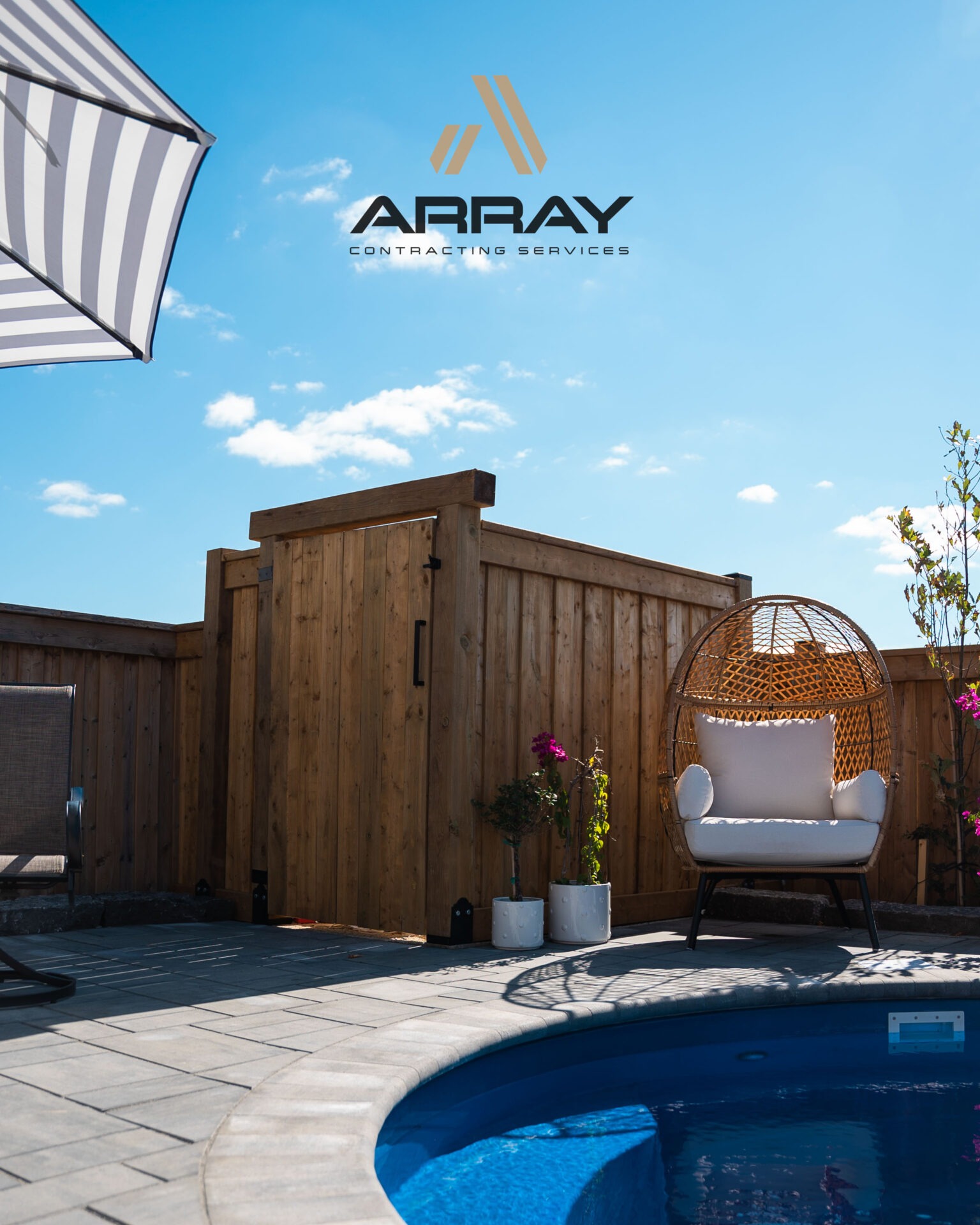 A backyard pool scene features a wicker chair, umbrella, and wooden fence under a clear sky, with the 