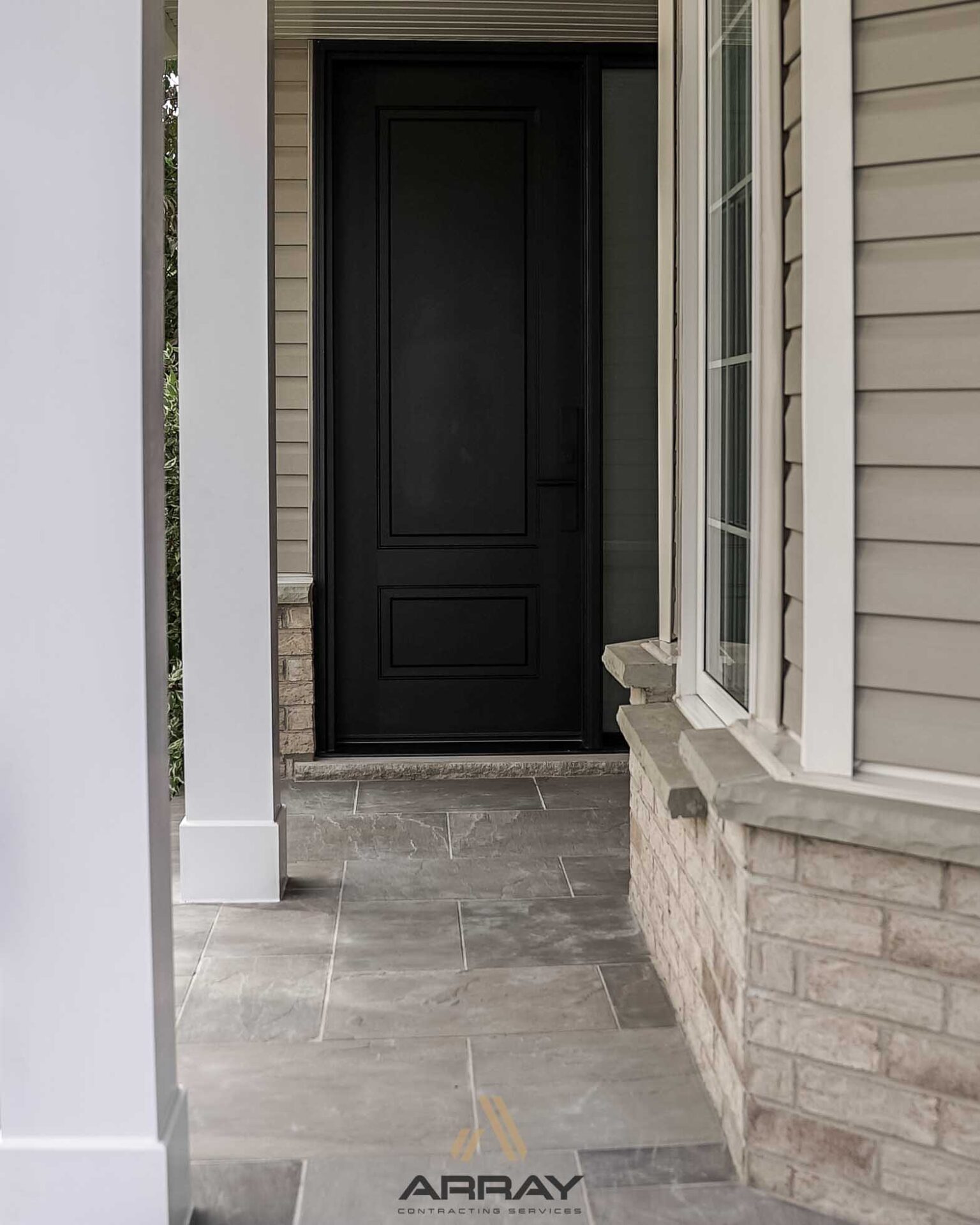 Modern entrance with dark door, light siding, and stone accents. Clean design featuring tiled flooring. No people or identifiable landmarks present.