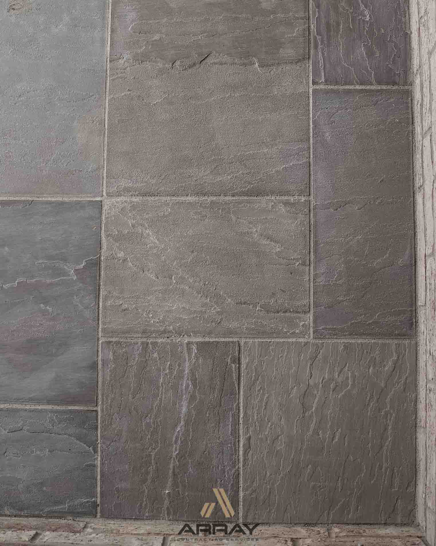 Close-up of a textured stone tile wall with grey and purple hues, showcasing an intricate design pattern and an 