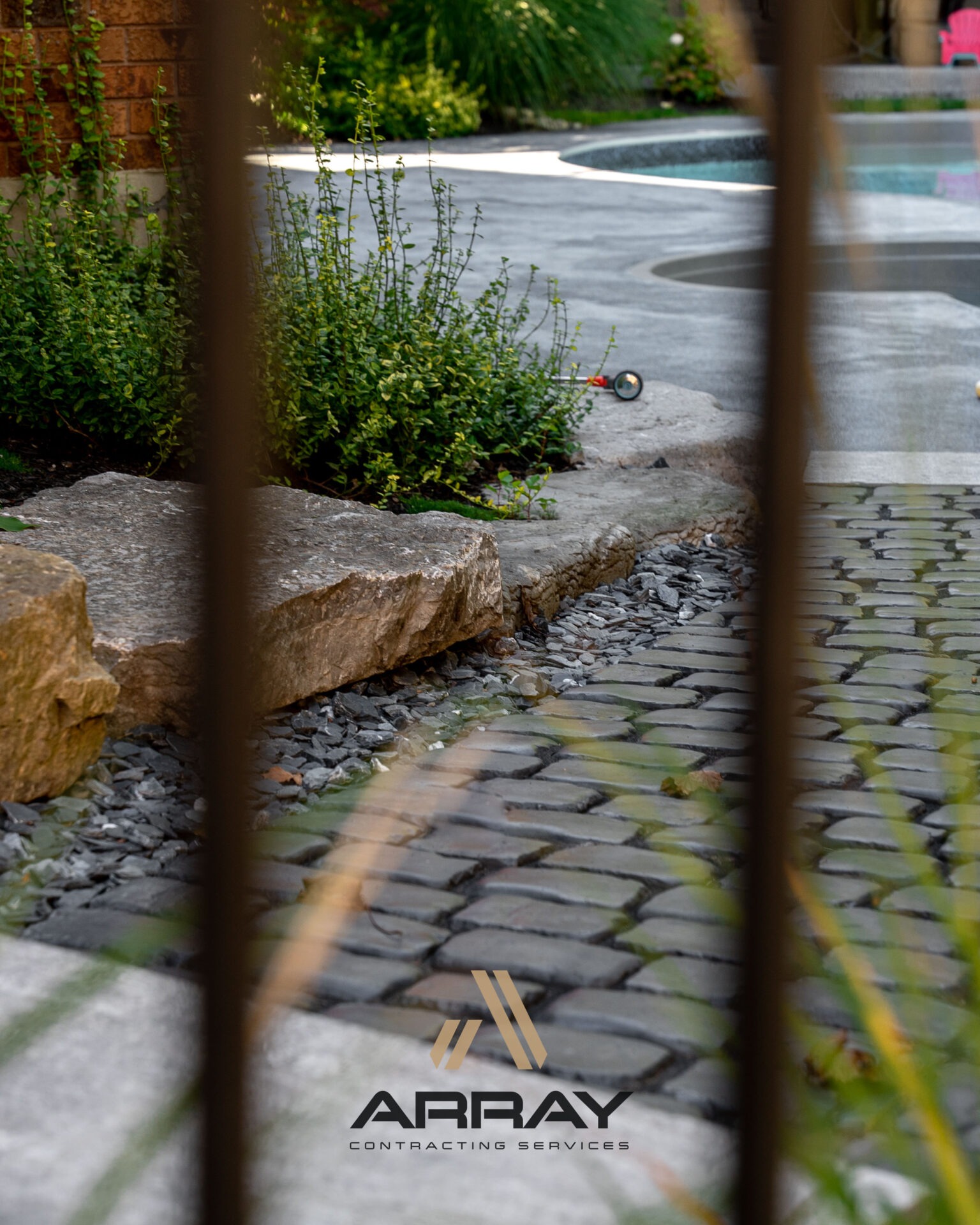 A landscaped backyard features a pool, stone pathway, and lush greenery. The image displays the logo of Array Contracting Services.