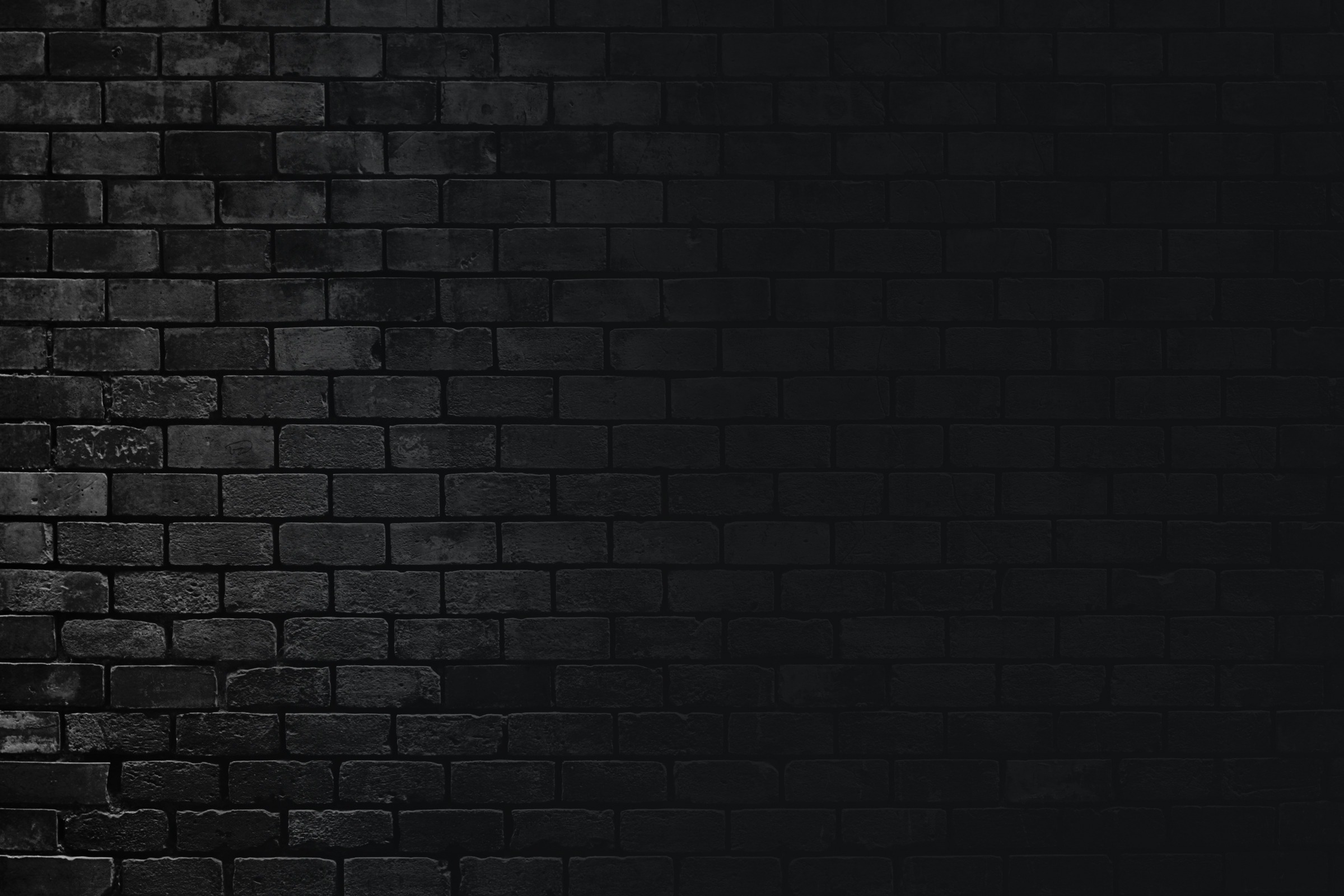 A dark brick wall with a subtle gradient lighting effect, creating a moody and atmospheric background suitable for various visual themes.