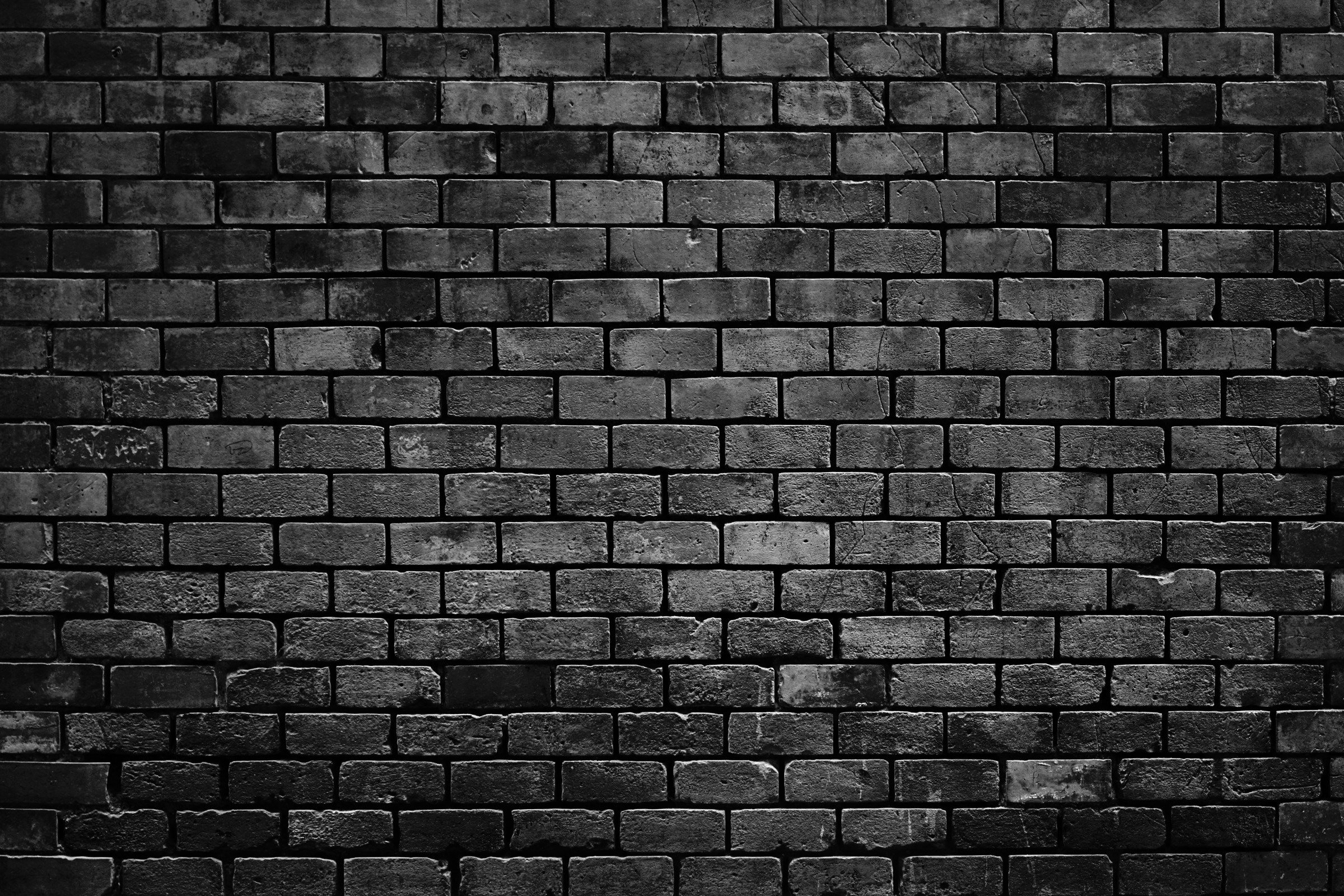 Dark, textured brick wall, showing wear and cracks. The monochrome tones emphasize the brick pattern, creating a moody, industrial atmosphere. No people present.