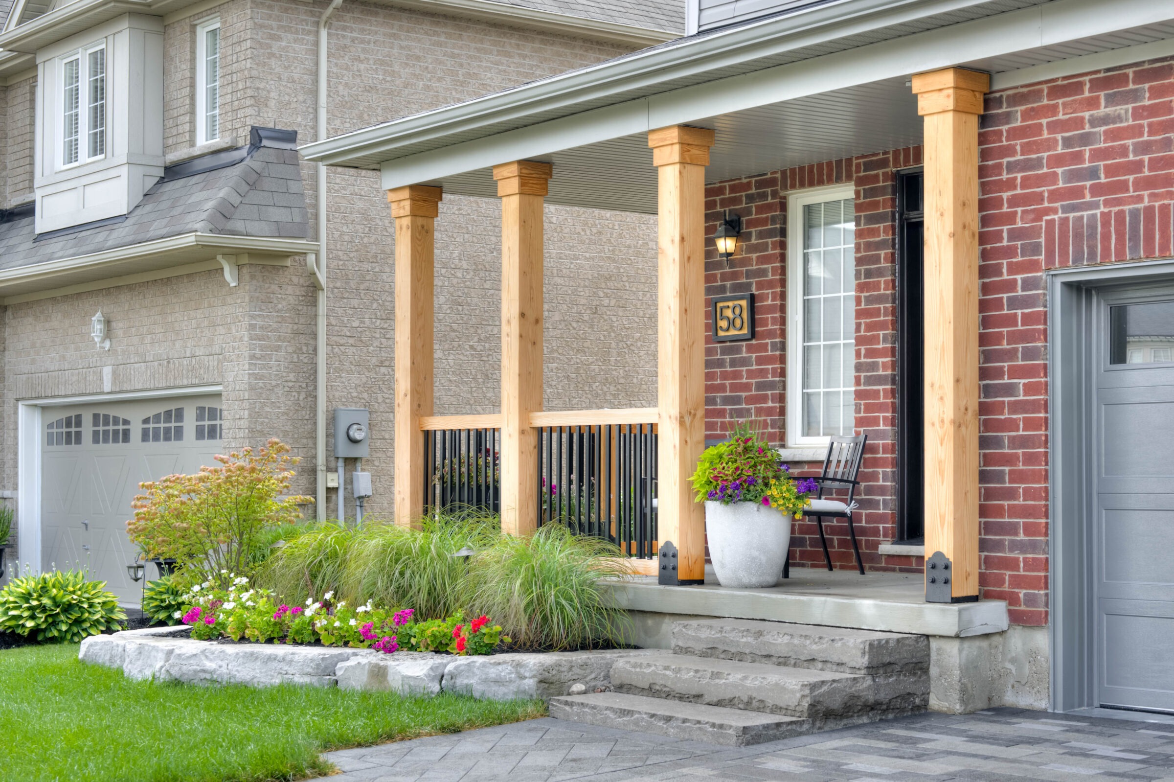 Brick house with a wooden porch, potted plants, and garden beside a concrete driveway. Features a chair and address number 58.