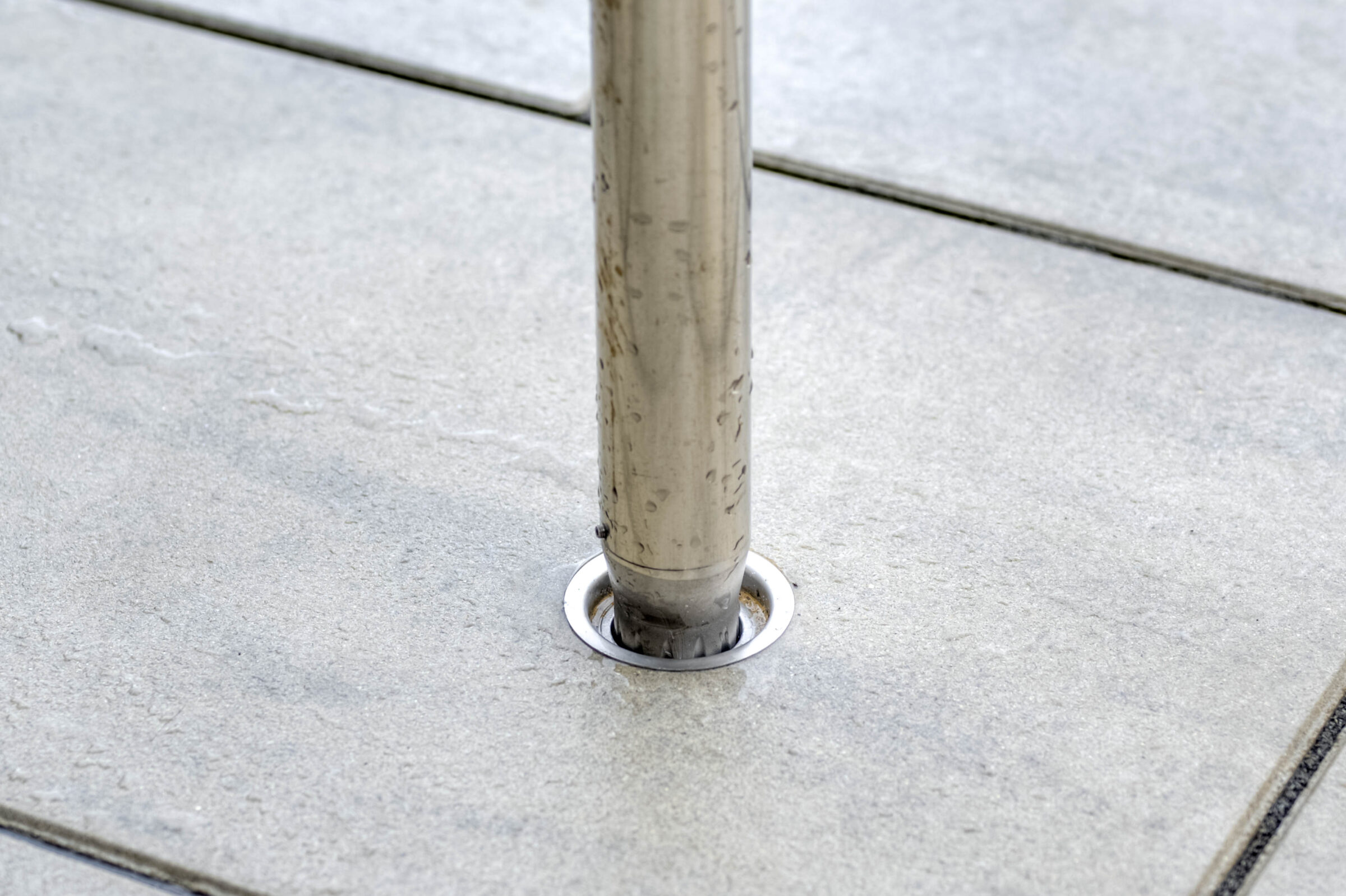 A metal pole is securely positioned in a concrete socket, surrounded by a smooth, gray tiled surface. Drops of water are visible.