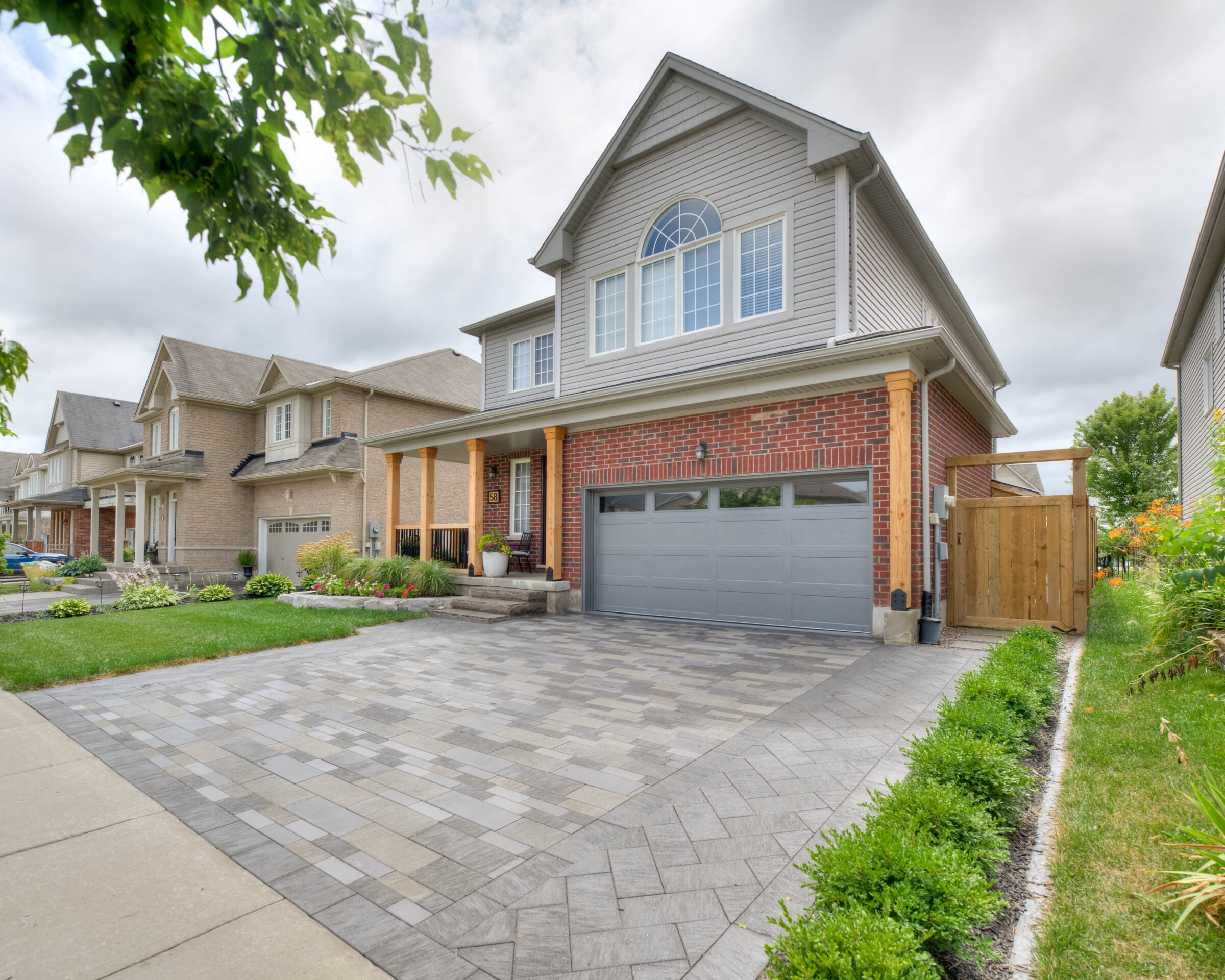 Suburban street with modern houses, tidy lawns, and a gray driveway. Overcast sky enhances the peaceful residential neighborhood scene. No people present.