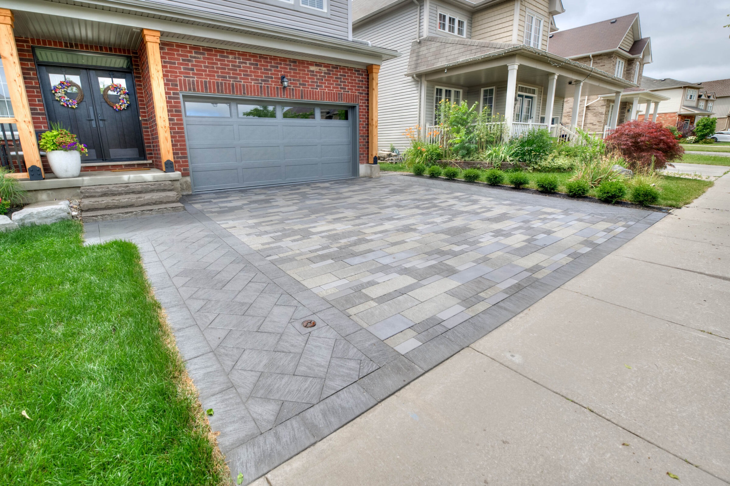 A modern suburban home with a brick facade, decorated porch, and patterned driveway, surrounded by well-maintained greenery and neighboring houses.