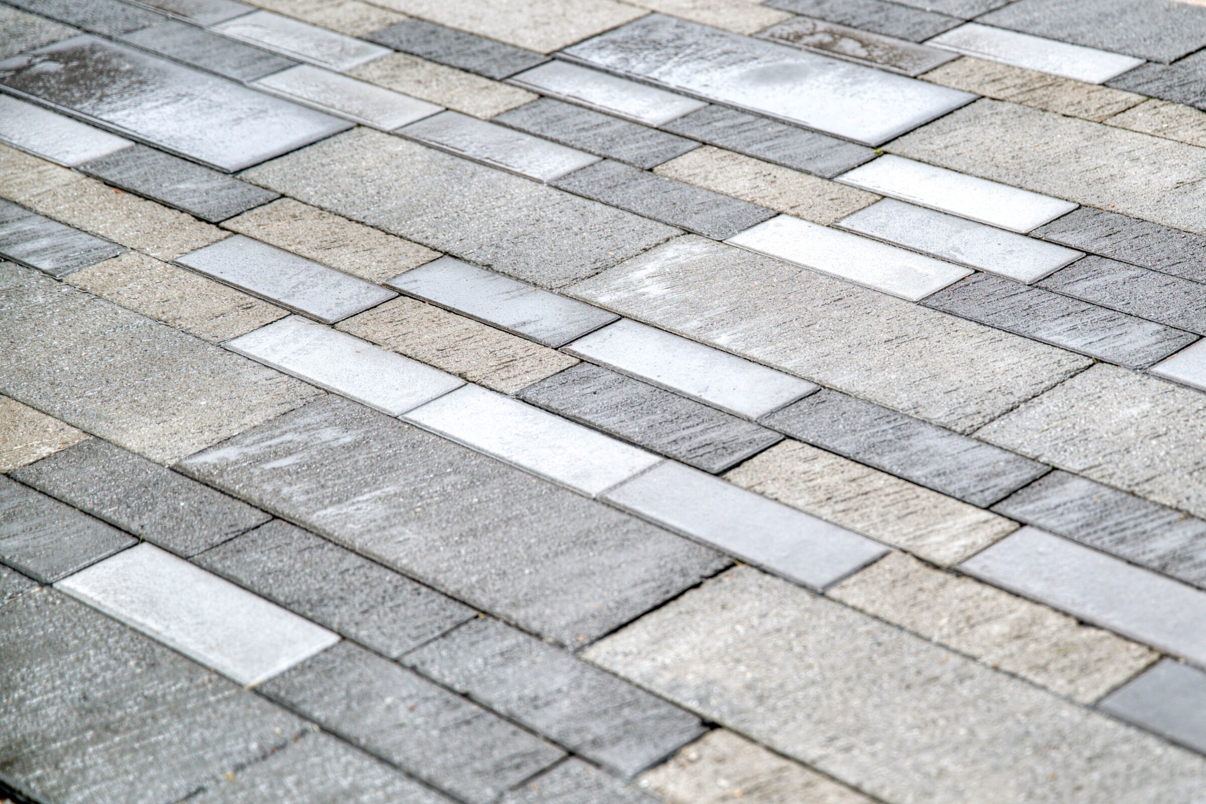 Close-up of a patterned stone pavement featuring varying shades of grey and white rectangular tiles arranged in an alternating, linear design.