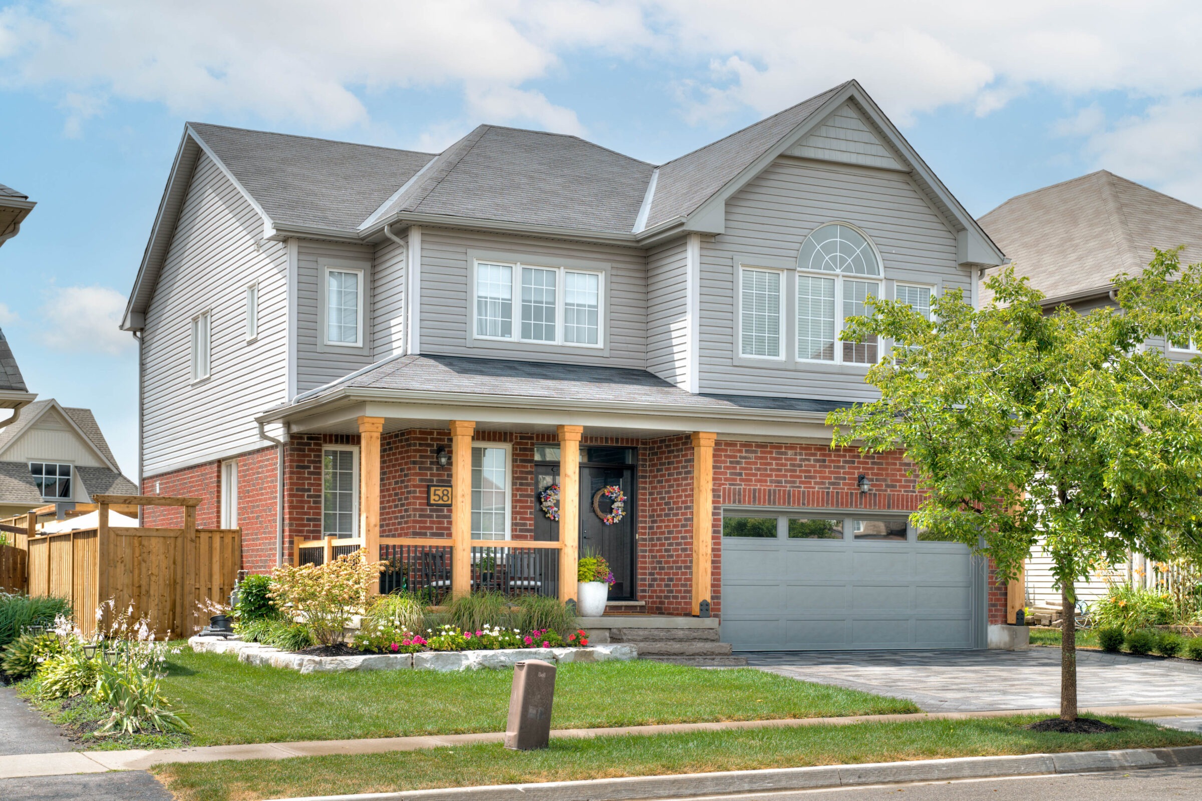 Two-story house with brick and siding exterior, landscaped front yard, and attached garage in a suburban neighborhood. Clear blue sky above.