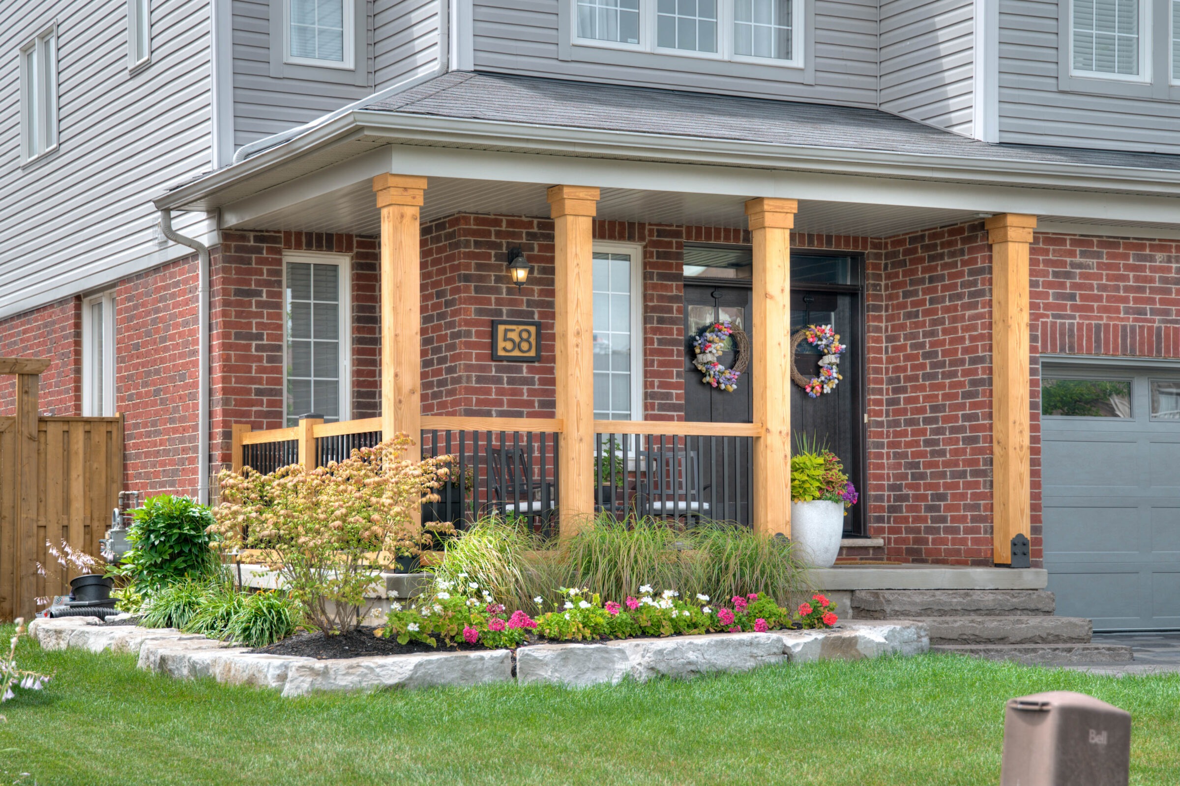 A brick house with a covered porch, wooden pillars, and colorful flowers in the garden, displaying welcoming charm and suburban tranquility.