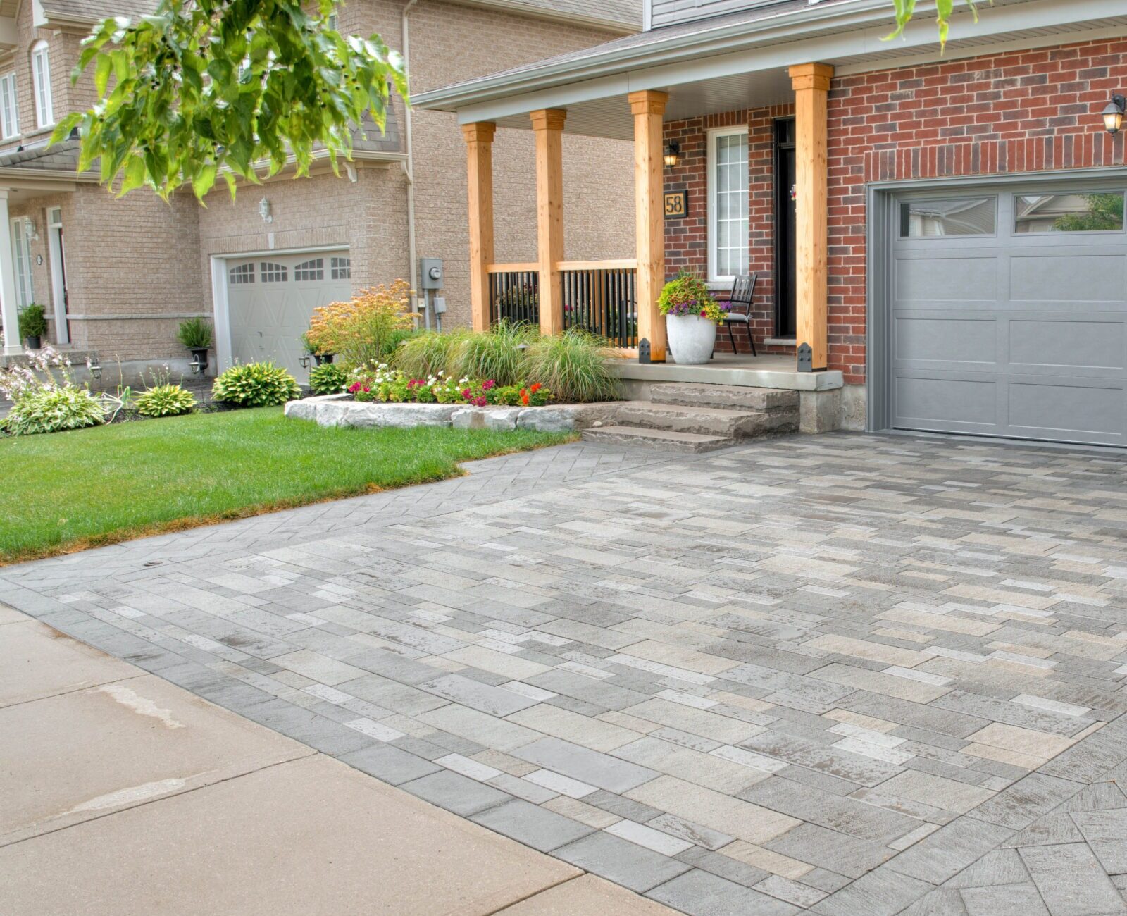 Brick house with a manicured front yard and paved driveway. Porch features planters and seating. No people or landmarks visible.