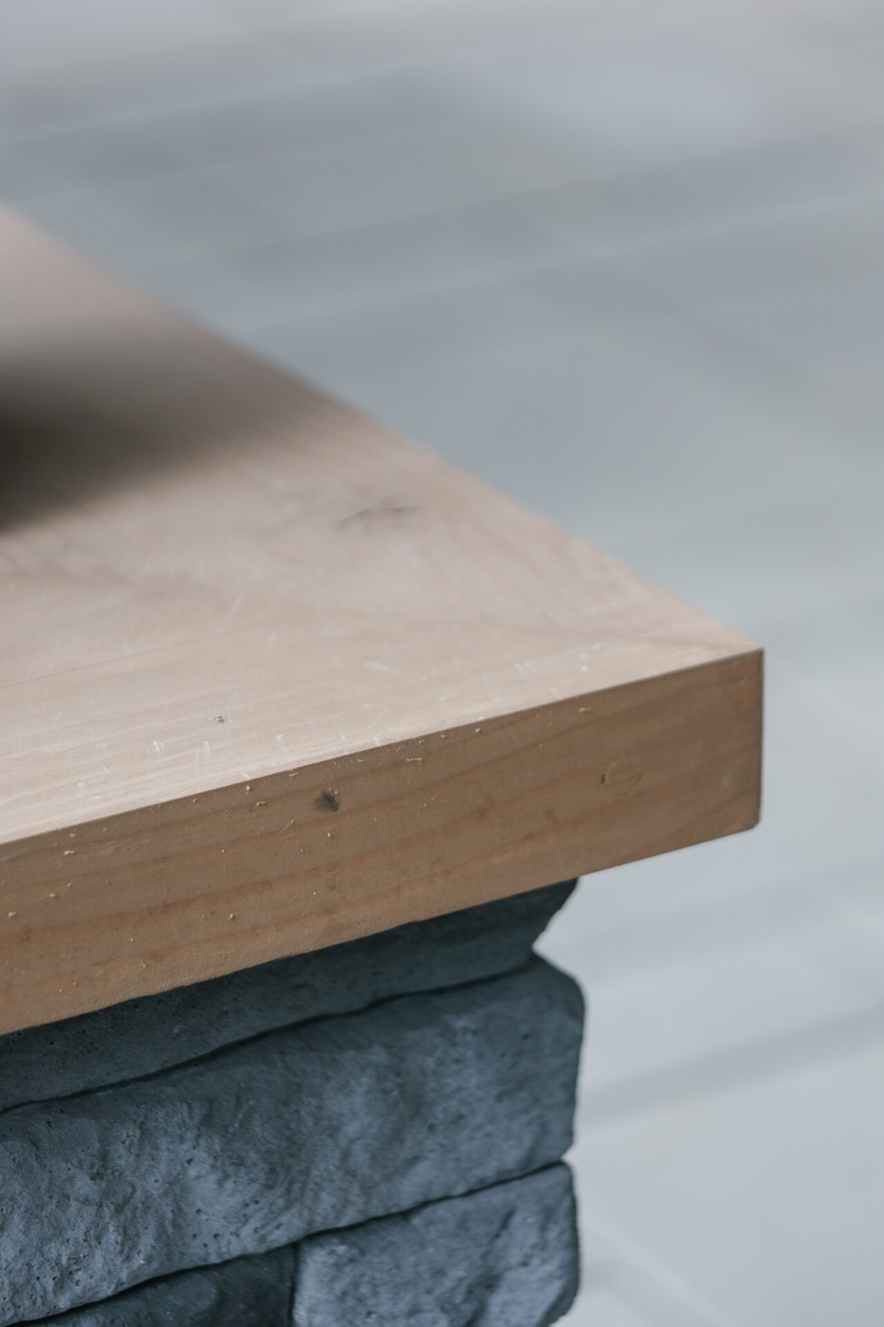 A close-up view of a thick, wooden slab resting on stacked, dark stone blocks with a smooth, tiled floor in the background.