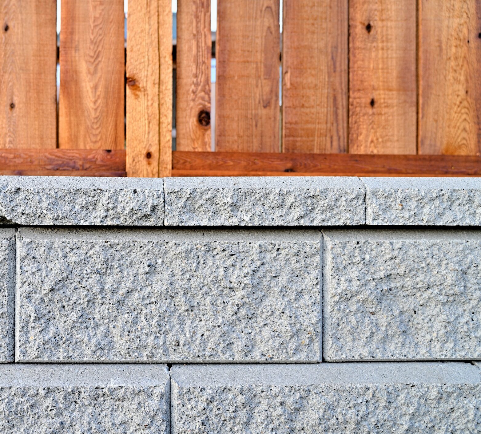 Gray concrete blocks form a textured wall, topped by a rustic wooden fence. The materials contrast in color and texture.