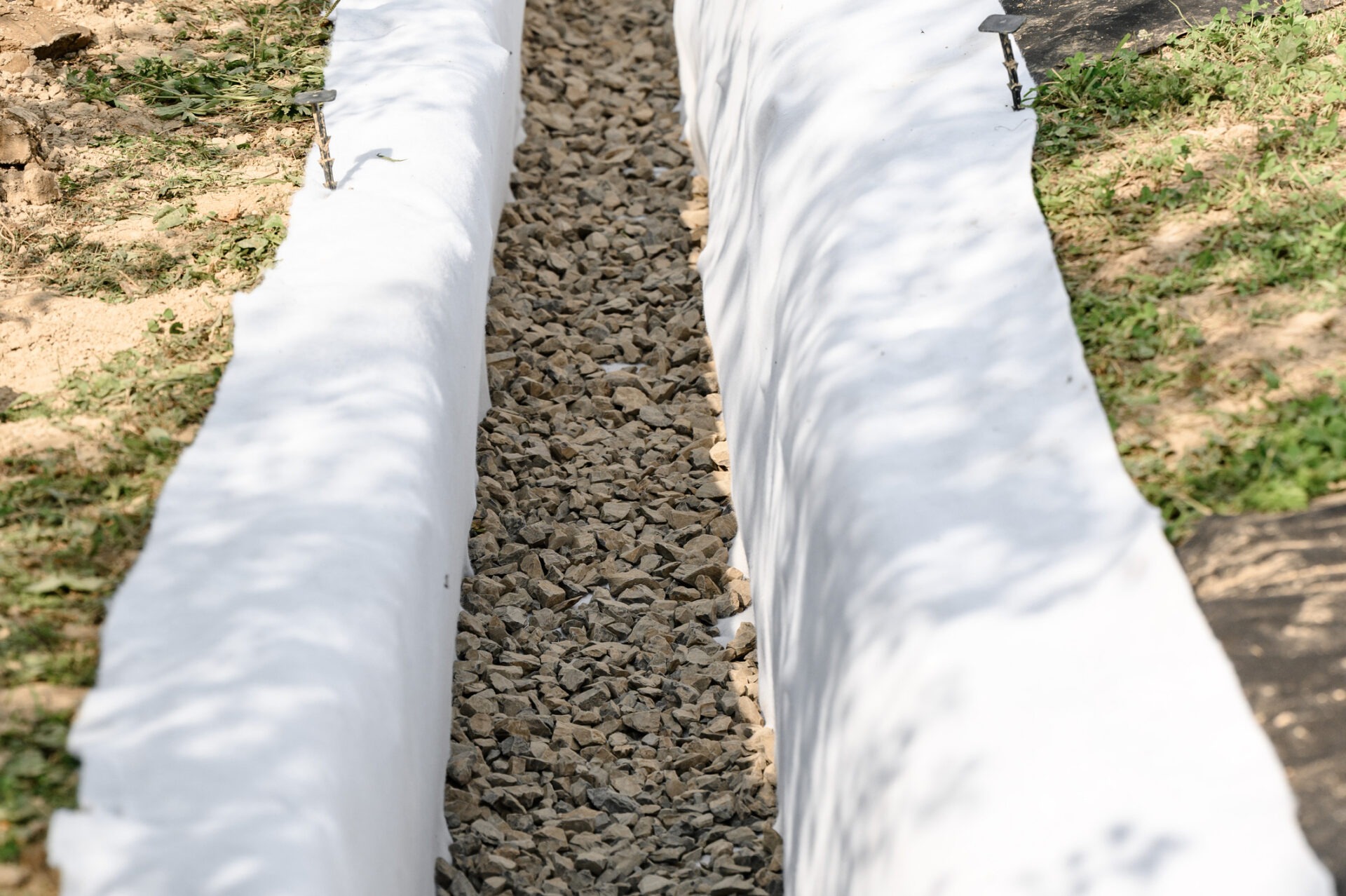 The drainage trench is covered with geotextile and filled with crushed stone to drain ground water from the site.
