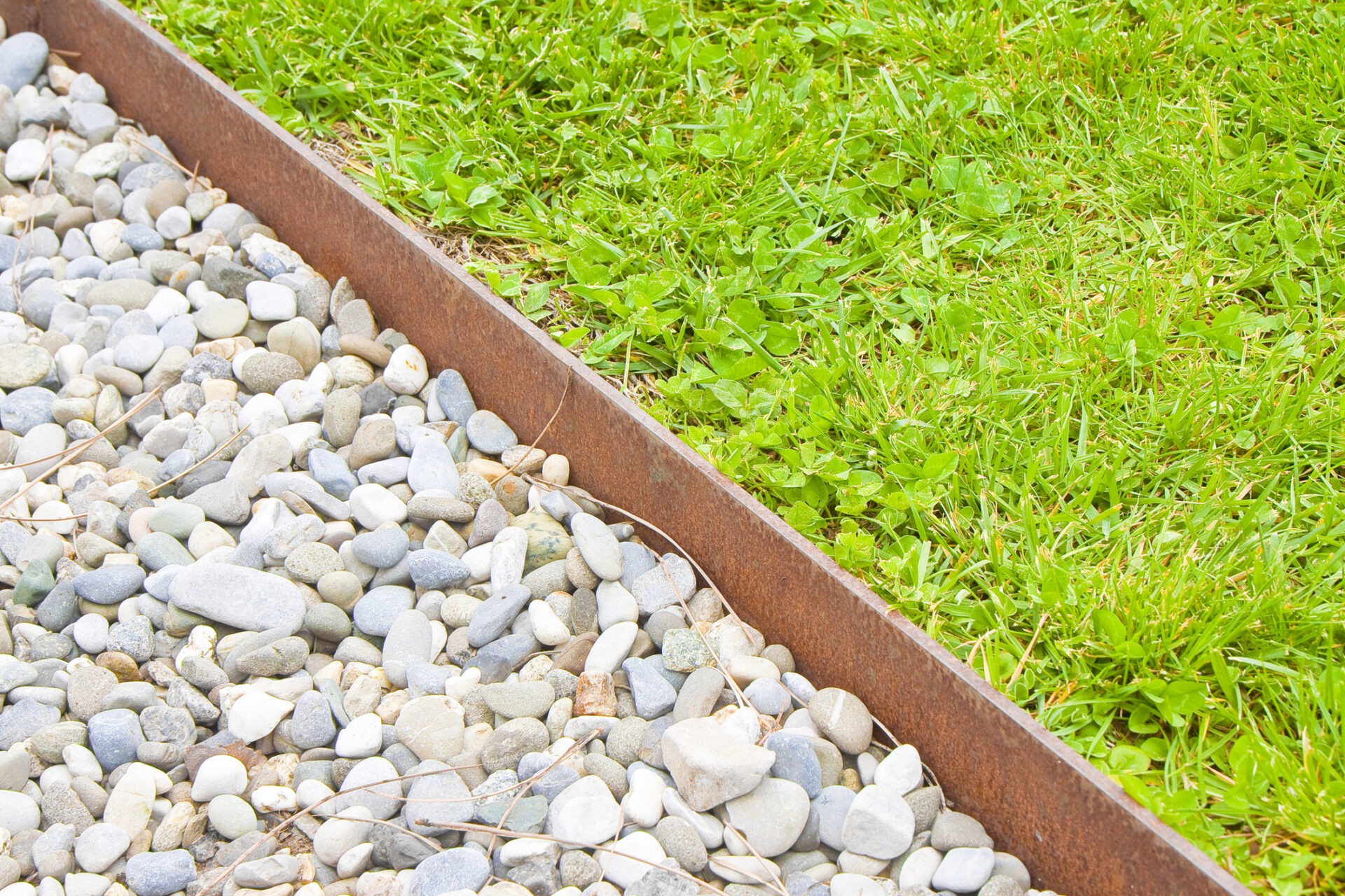 White gravel floor and fresh green lawn with clovers and rusty metal containment profiles